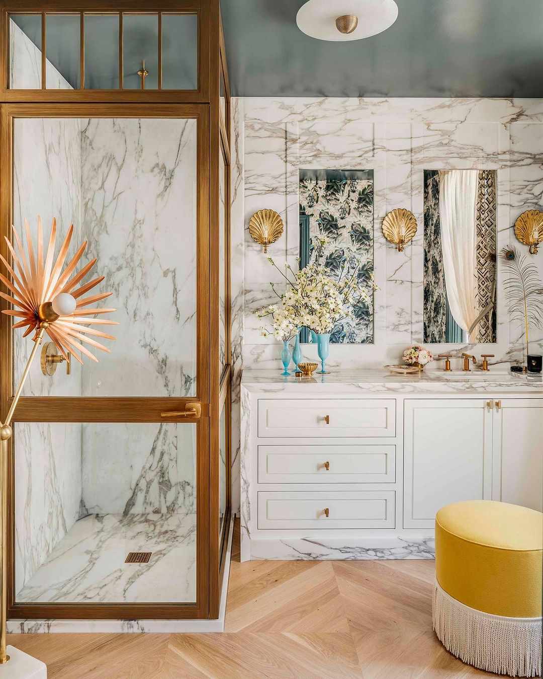 Baño de inspiración parisina con paredes de mármol, techo cerceta y otomana amarilla