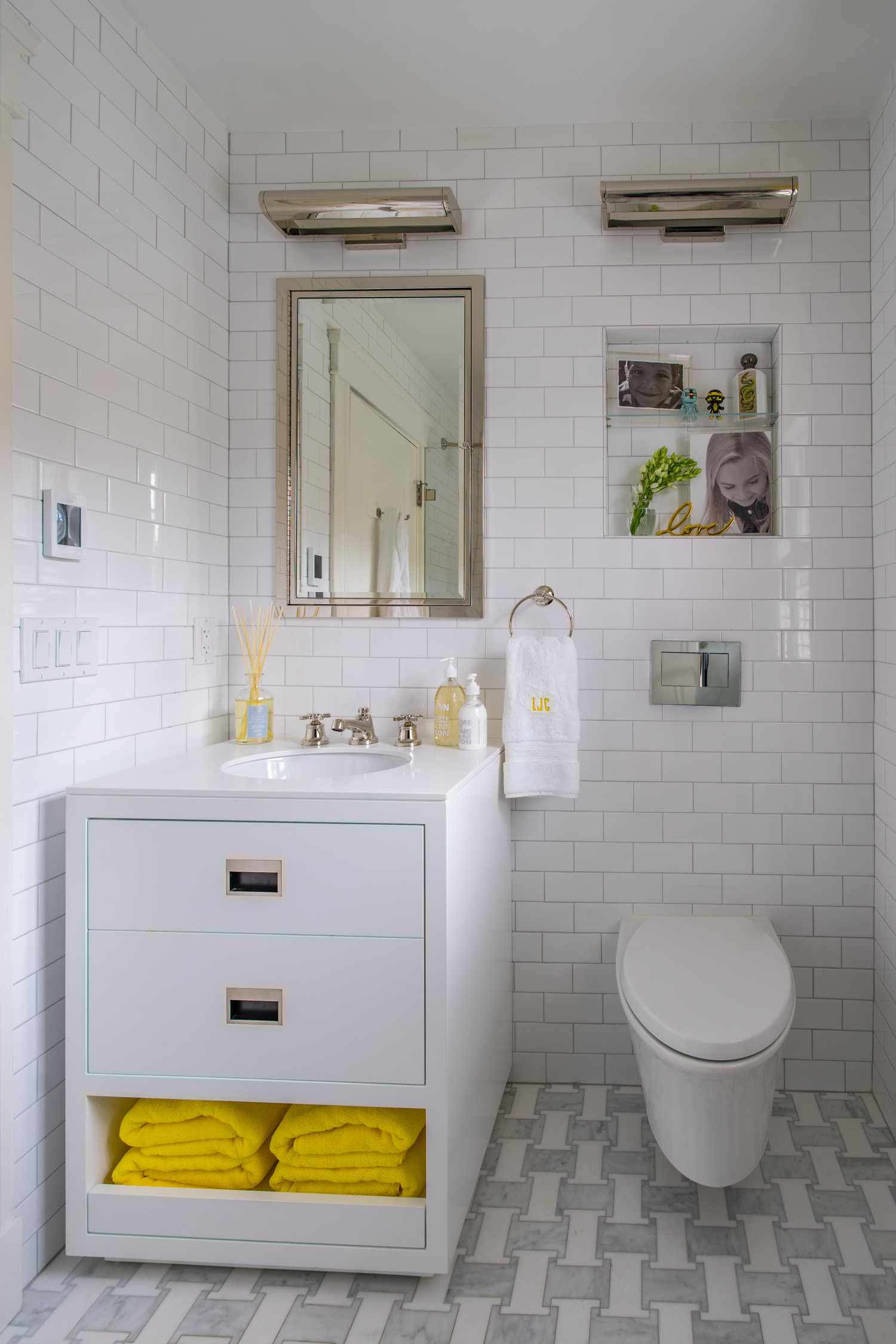 Baño blanco con azulejos de metro, accesorios cromados y toallas y accesorios amarillos 
