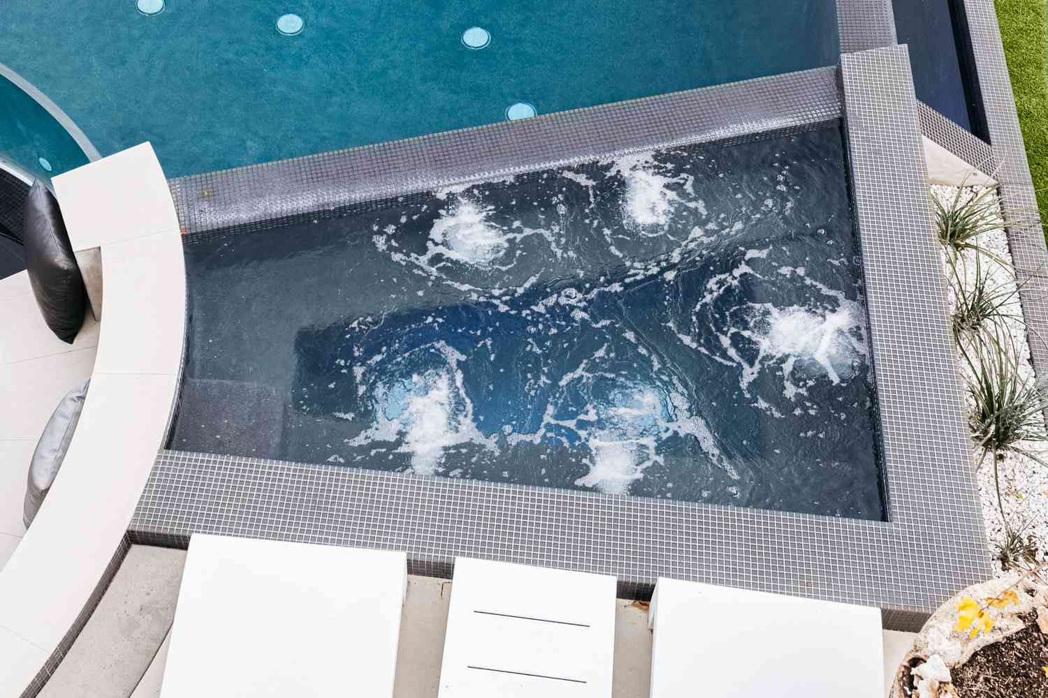 Banheira de hidromassagem moderna ao lado de cadeiras reclináveis brancas e piscina
