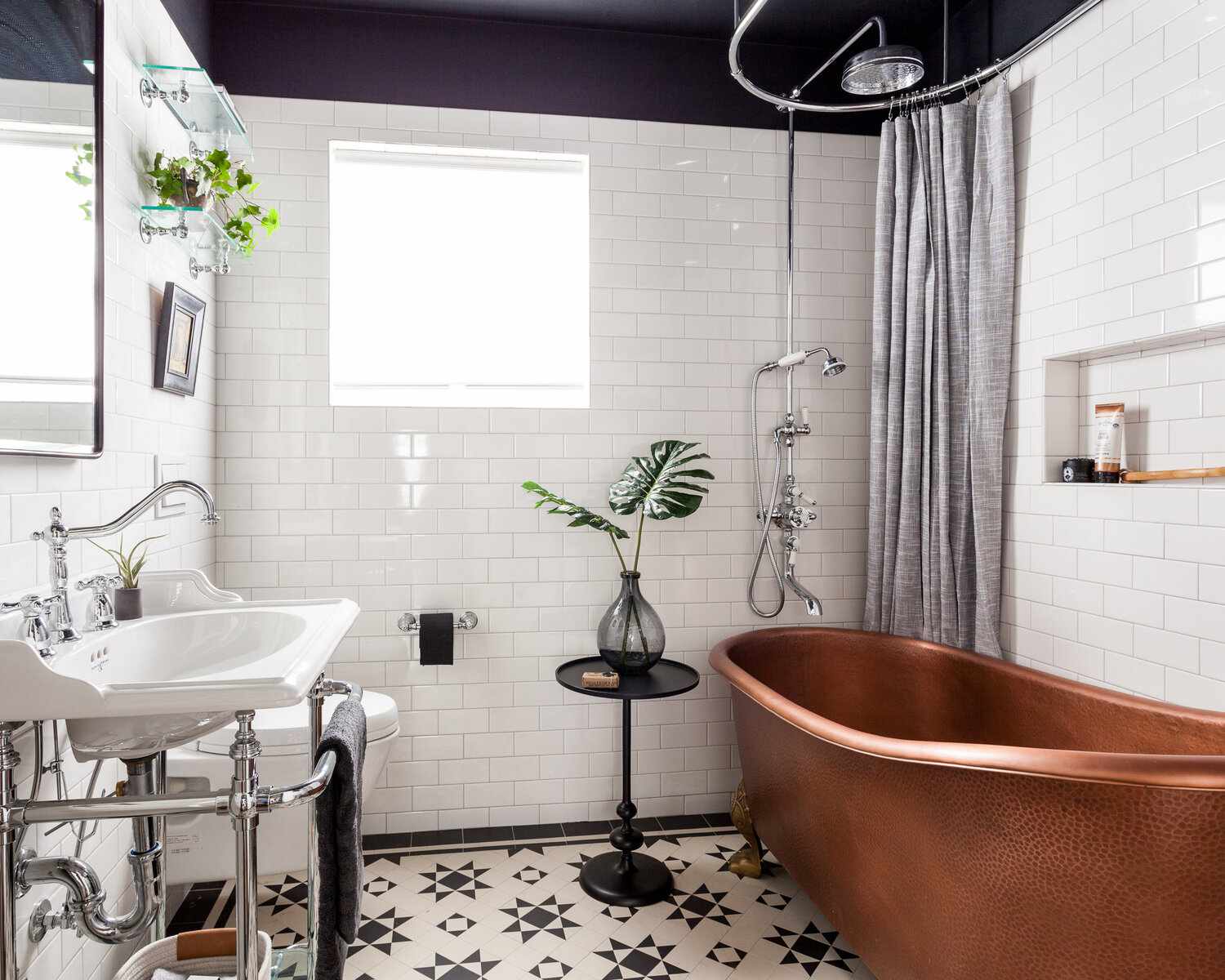 Um banheiro primário pequeno e marcante com piso de azulejos arrojados, uma banheira com pés de garra de cobre e várias prateleiras de vidro