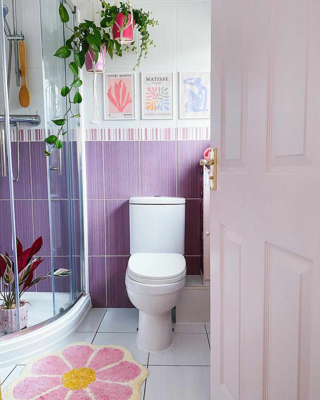 Banheiro em tons pastéis com azulejos roxos na parede.