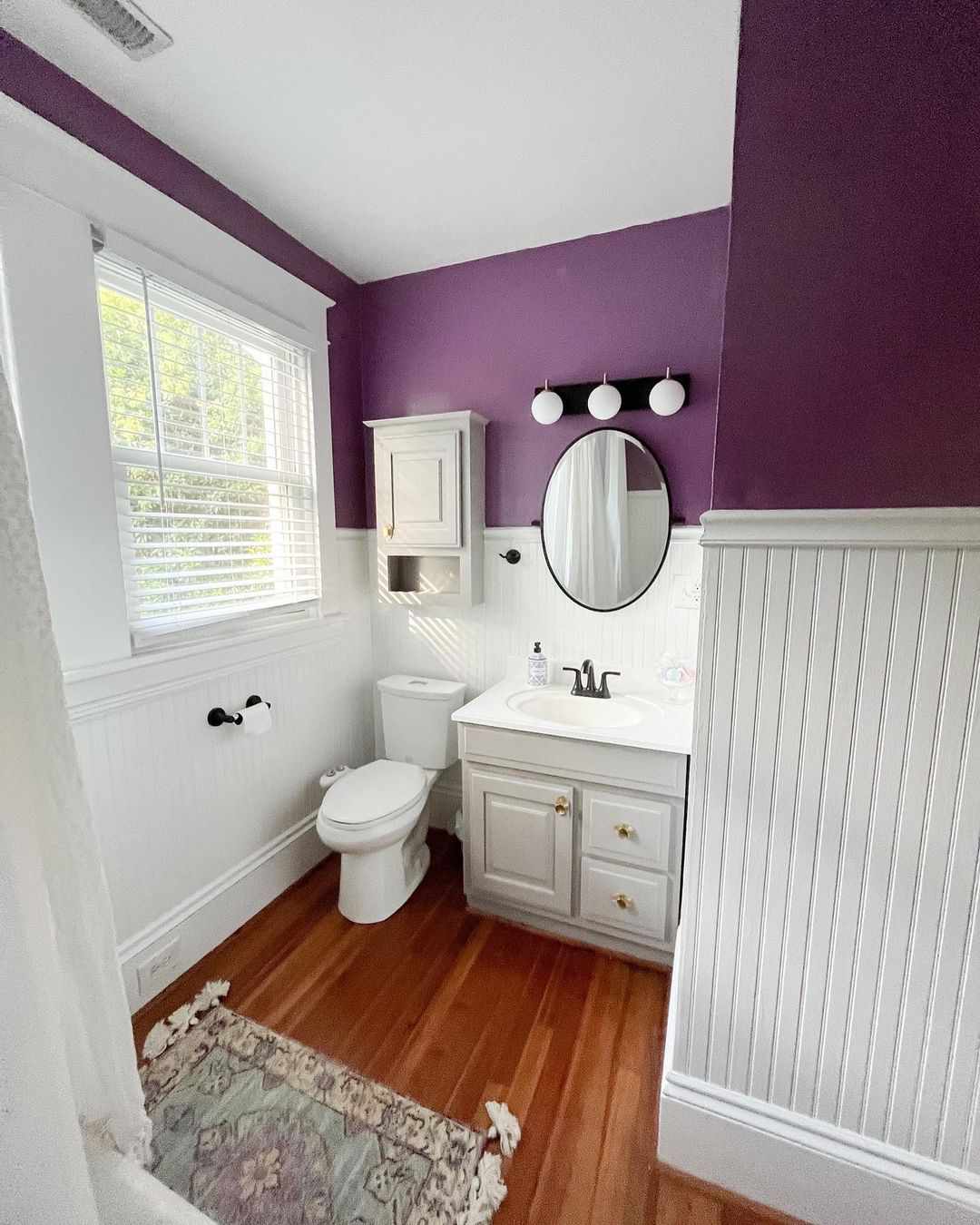 Cuarto de baño con paneles de pared blancos y pintura morada.