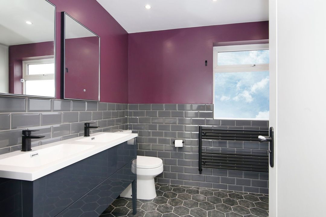 Banheiro grande com azulejos cinza e pintura de parede roxa.