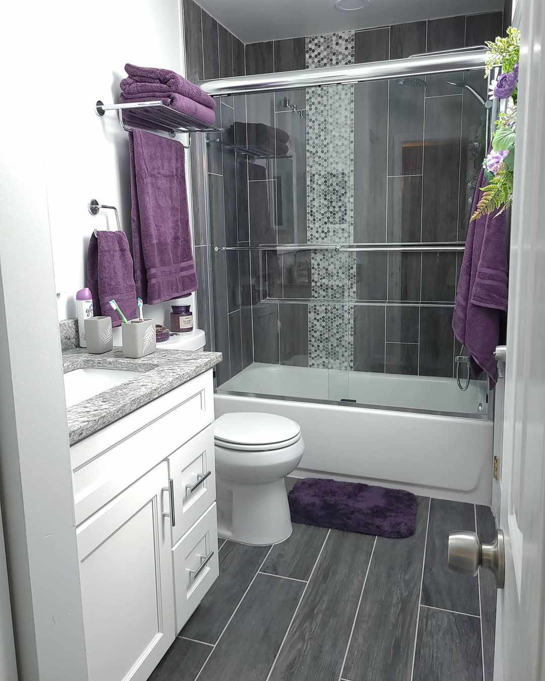 Baño gris y blanco con toallas moradas.