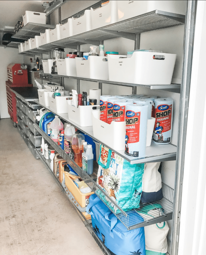 Una colección de cubos blancos llenos de artículos para el hogar a granel se alinean en un garaje