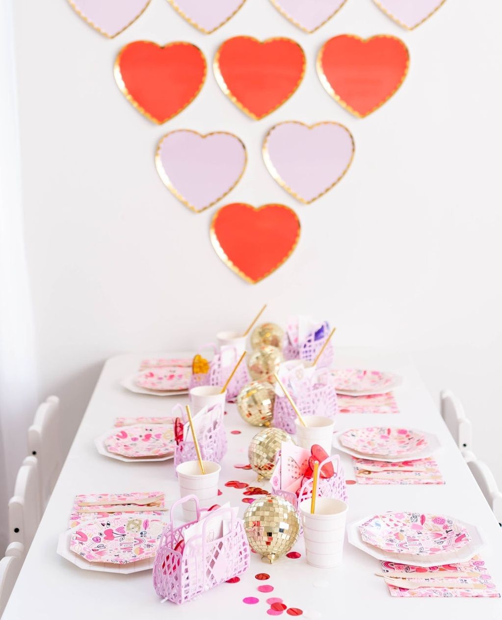 Platos de corazones rosas y rojos en la pared sobre una mesa blanca y rosa