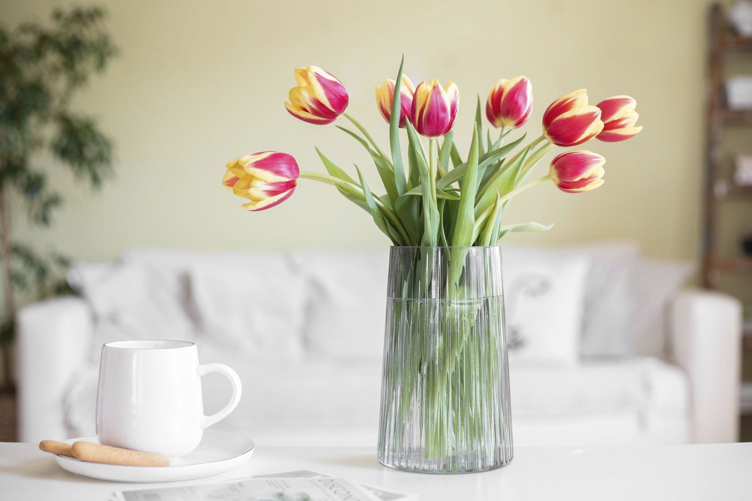 Tulipas cortadas em amarelo e rosa colocadas em um vaso de vidro ao lado de uma caneca de café