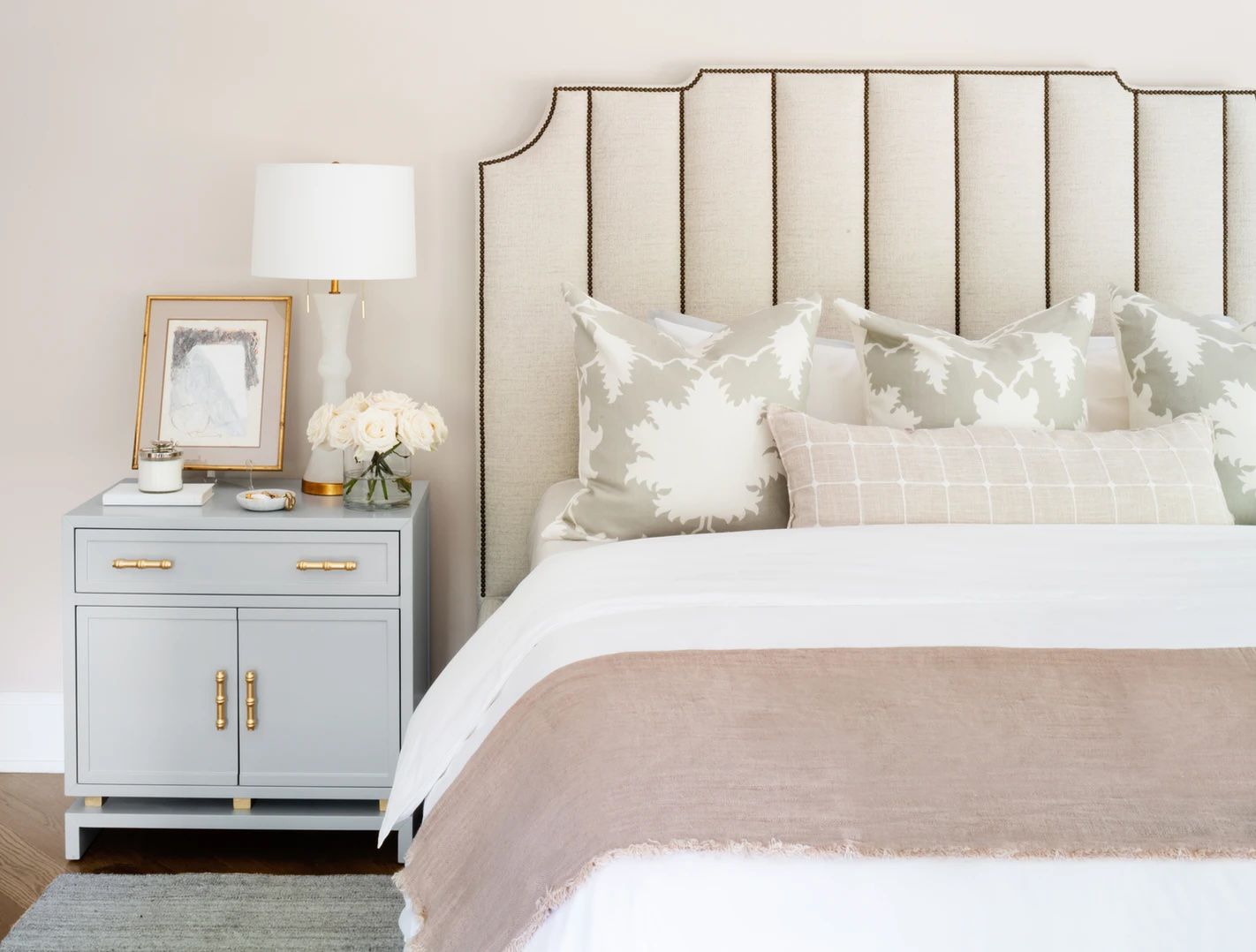 Chambre à coucher avec table de nuit bleu clair et un lit rembourré avec literie blanche et accents roses poussiéreux